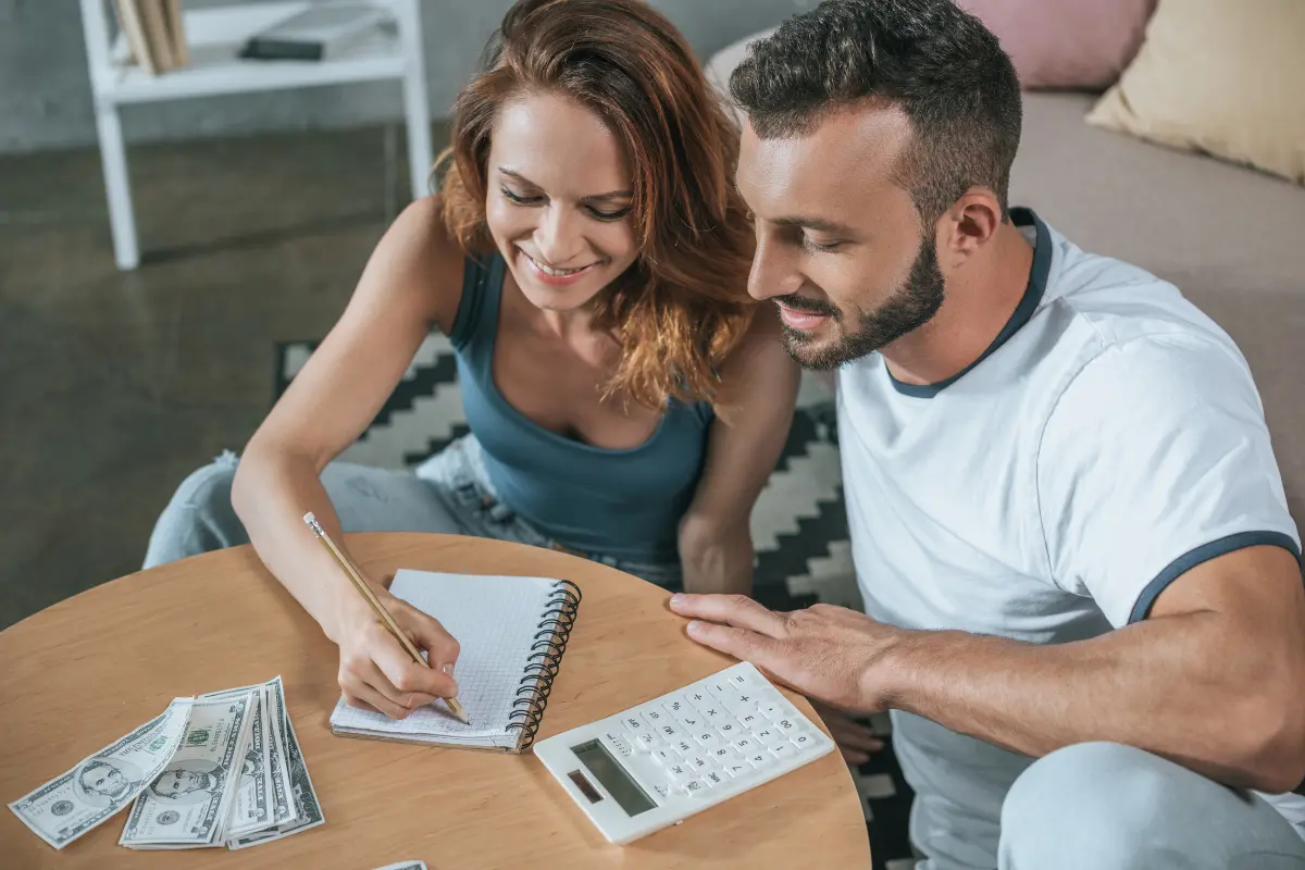 Couple Organizing Expenses With Calculator And Notebook While Applying Money Saving Tips For Your Wedding To Stay Within Their Planned Budget