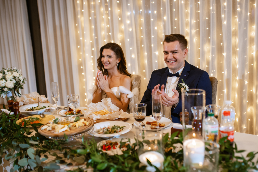 Bride and groom smiling during their reception dinner at a decorated ballroom.
