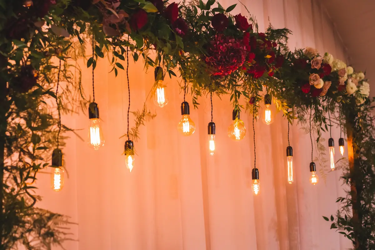 Overhead Greenery And Warm Hanging Lights Illustrating Modern Indoor Wedding Decoration Ideas Focused On Atmosphere And Layered Lighting