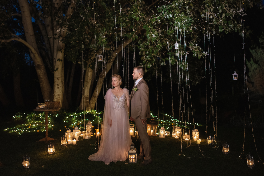 Newlyweds in garden with lanterns and string lights, romantic reception theme.