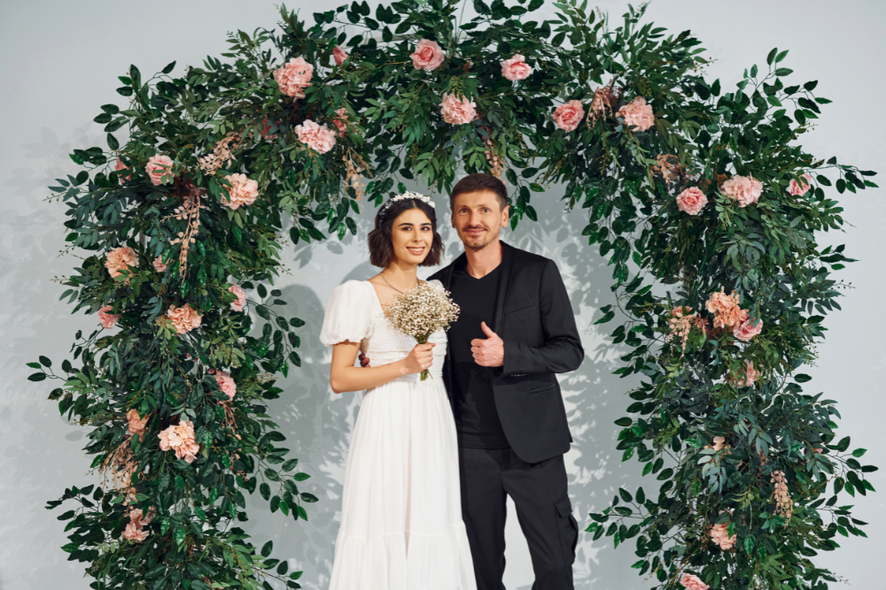 Bride and groom posing under a floral arch, showcasing 2025 wedding trends with bold floral décor.